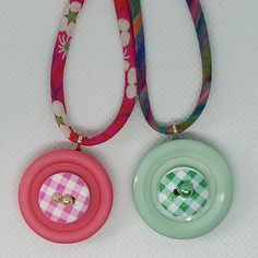 two necklaces with buttons attached to them on a white tablecloth background, one is pink and the other is green