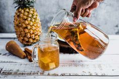 a person pouring tea into a glass pitcher next to a pineapple and cinnamon sticks