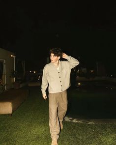 a man standing in the grass with his hands on his head while wearing a button up shirt and khaki pants