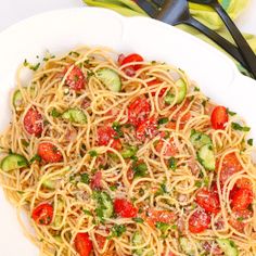 a white bowl filled with pasta and vegetables on top of a table next to utensils