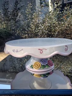 there is a cake stand that has flowers on it and letters painted on the top