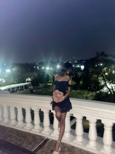 a woman in a short dress is standing on a balcony at night with her hands behind her back