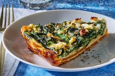 a slice of quiche with spinach and cheese on a plate next to a fork