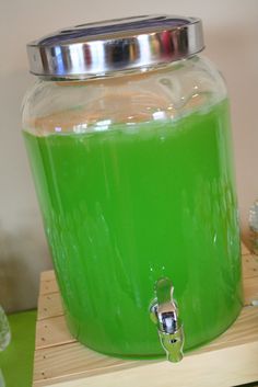 a green liquid in a glass jar with a metal lid sitting on a wooden stand