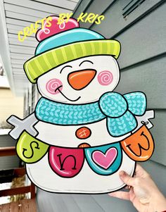 a hand holding up a snowman cutout on the side of a house with words written below it