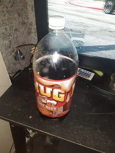 a large bottle of liquid sitting on top of a black table next to a window