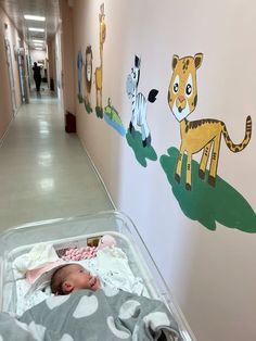 a baby laying in a crib next to a wall with animals painted on it