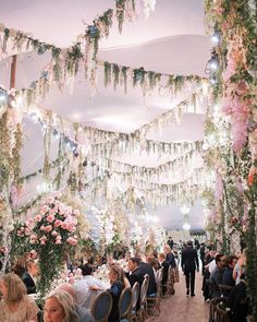 people are sitting at tables with flowers hanging from the ceiling