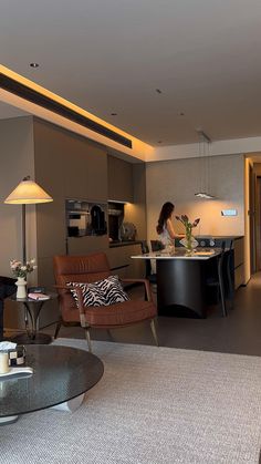 a living room filled with furniture and a woman standing in the kitchen next to it