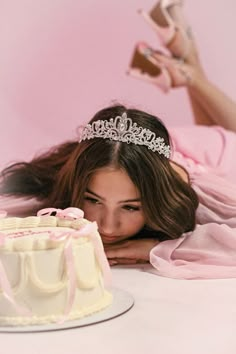 a woman laying next to a cake with a tiara on it's head