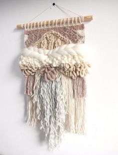 a wall hanging made out of yarn and wood sticks with white, pink, grey and beige colors