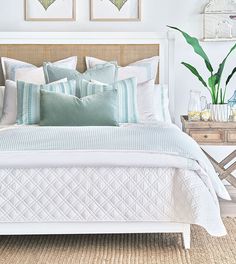 a white bed with blue and green pillows in a bedroom next to two planters