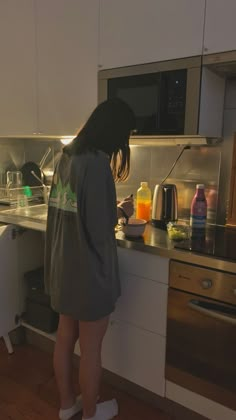 a woman is standing in the kitchen preparing food on the counter top and looking into the oven