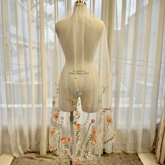 a mannequin is standing in front of sheer curtains with flowers on the sides