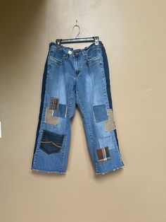 a pair of blue jeans with patches on them hanging from a clothes hanger against a wall