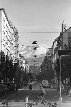 a man riding a bike down the middle of a street next to tall buildings and mountains