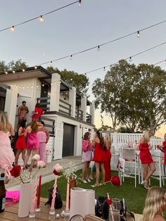 a group of women in pink dresses standing on top of a grass covered field next to a white house