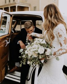 a bride and groom sitting in the back of an old car with their wedding bouquet