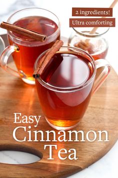 two mugs filled with cinnamon tea on top of a wooden cutting board