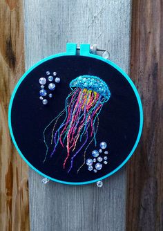 an embroidered jellyfish is hanging on a wooden fence with bead work in the hoop