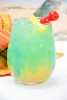 a blue and yellow drink with a cherry on the top sitting next to a towel