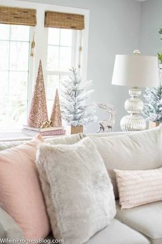 a living room filled with white furniture and christmas trees on top of the couches