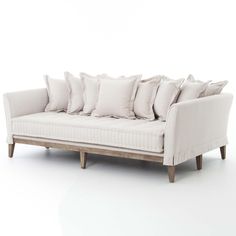 a white couch with many pillows on it's back and legs, sitting in front of a white wall