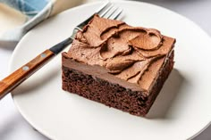 a piece of chocolate cake on a white plate with a knife and fork next to it