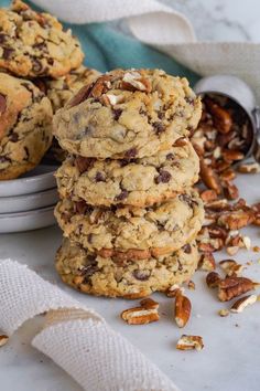 chocolate chip cookies stacked on top of each other with pecans scattered around the edges