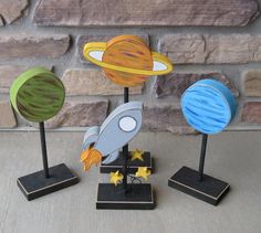 three small wooden planets are on display in front of a brick wall, and one has a rocket ship