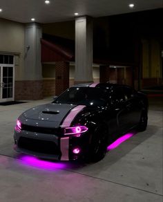 a black and pink sports car parked in front of a building with its lights on