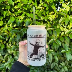 a person holding up a cup with a sticker on it in front of some bushes