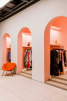 an orange chair sitting in front of a pink wall and some shelves with clothes on them