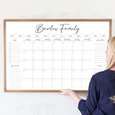 a woman pointing to a family calendar on a whiteboard in front of a wall