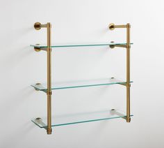 three glass shelves with brass fittings against a white wall