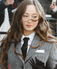 a woman with long hair wearing a gray jacket and black tie is posing for the camera