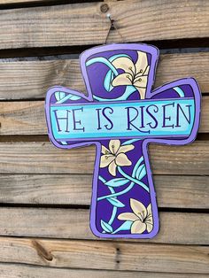 a wooden cross with the words he is risen on it and flowers painted on it