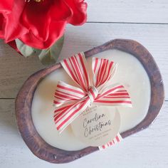 a candle with a red bow on it next to a flower in a wooden bowl