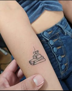 a woman's arm with a small tattoo of a stack of books on it