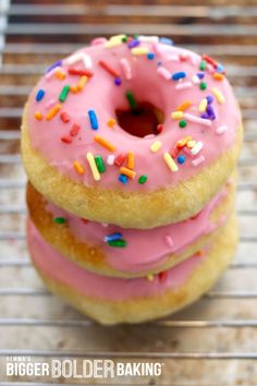 three donuts with pink frosting and sprinkles on a cooling rack