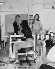 three women are sitting in a room and one woman is holding a camera while the other sits on a chair