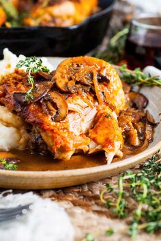 a plate topped with meat and mushrooms covered in gravy on top of mashed potatoes