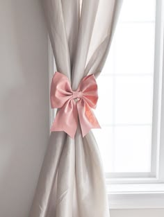 a pink bow hanging on the side of a white curtain in front of a window