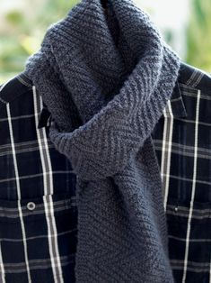 a close up of a person wearing a gray sweater and a black plaid shirt with a scarf around his neck