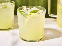 two glasses filled with lemonade and ice sitting on a table next to each other