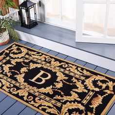 a black and gold door mat with the letter b on it next to a potted plant