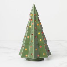 a small green ceramic christmas tree on a white table with red, yellow and orange ornaments