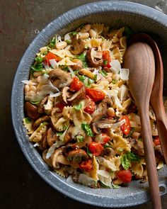 a bowl filled with pasta and vegetables next to a wooden spoon on top of a table