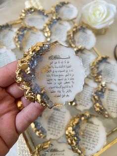 a hand holding a piece of glass with writing on it and flowers in the background