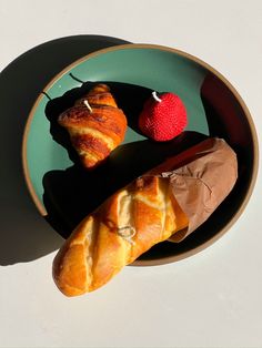 two croissants on a plate with a strawberry in the bowl next to them